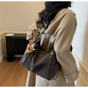 Détail du sac à bandoulière marron mat avec breloque en peluche et accents de fermeture éclair