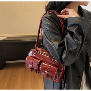 Detail of burgundy retro Boston bag with shiny leather and front buckle pockets on a model