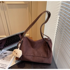Detail view of dark brown suede shoulder bag with a plush charm on a leather stool