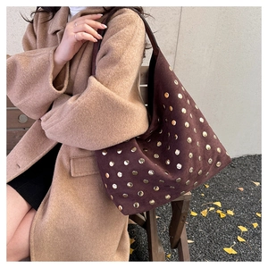 Brown suede tote bag with golden studs shown on model in a scenic autumn setting