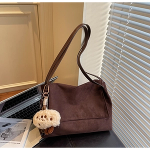 Detail of a dark brown suede tote bag featuring a plush charm and slender shoulder strap