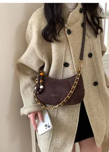 Détail du sac demi-lune en daim marron foncé avec chaîne dorée et breloque perlée