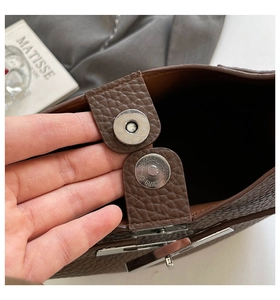 Detail of magnetic snap closure and silver twist lock on brown pebble leather bucket bag