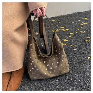 Detail of olive green suede hobo bag with gold studs on autumn leaf background