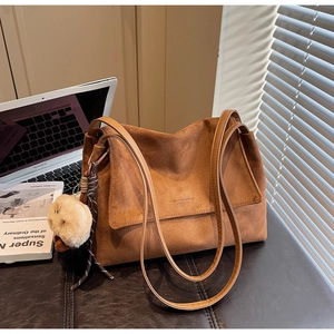 Brown suede tote bag detail with plush charm and braided tassel in a cozy setting