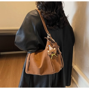 Détail d'un sac cabas en cuir marron vintage avec fermeture à franges et charme d'ours
