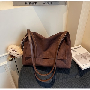 Detail of dark brown suede tote bag featuring dual straps and a cute plush doll charm