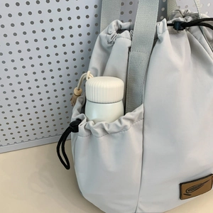 Detail of grey nylon tote bag showing side drawstring pocket with small water bottle
