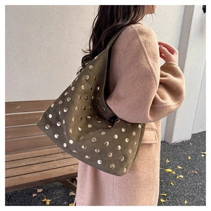 Deep olive green suede tote bag with golden rivets shown in an outdoor lifestyle setting