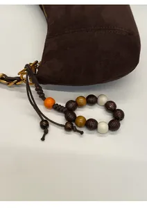 Détail d'un sac en daim marron foncé avec chaîne dorée et pendentif en perles de bois