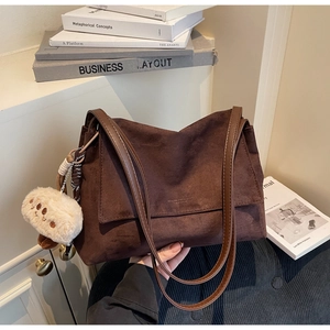 Close-up of brown suede tote bag with embossed logo and cute white plush bear charm