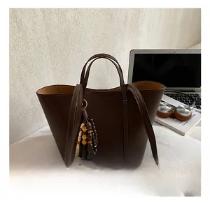 Close-up of a large dark brown faux leather tote bag with a vintage wooden bead charm accessory