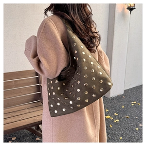 Detail of dark olive suede hobo bag with vintage metal rivets worn over a beige coat