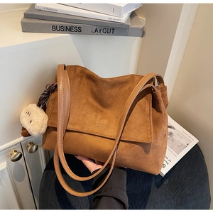 Detail of a brown suede tote bag featuring double shoulder straps and a cute plush bear charm
