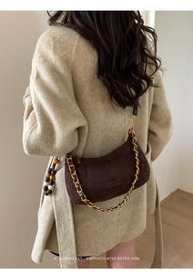 Détail du sac demi-lune en daim marron foncé avec chaîne dorée et perle en bois sur mannequin