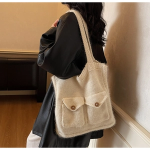Close-up of cream knit tote bag showing textured stitch details and dual front button pockets