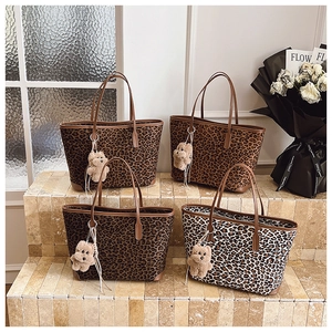 Detail view of four leopard print canvas tote bags with cute plush bear charms on stone steps
