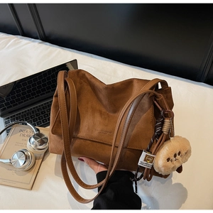 Close-up of caramel suede tote bag detail with plush bear charm and embossed logo