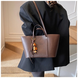 Dettaglio di una borsa tote grande in ecopelle marrone con ciondolo etnico in legno