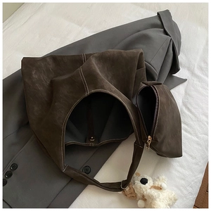 Detailed view of large dark brown suede tote bag with white stitching and plush charm