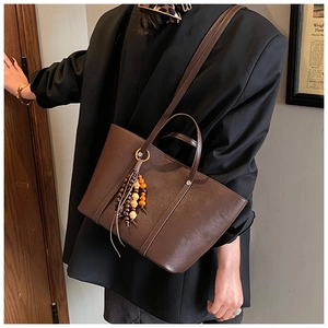 Detail of dark brown tote bag featuring retro wooden bead tassels and smooth leather texture