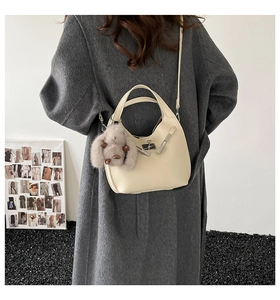 Detail view of cream lychee leather bucket bag featuring silver lock and dog charm