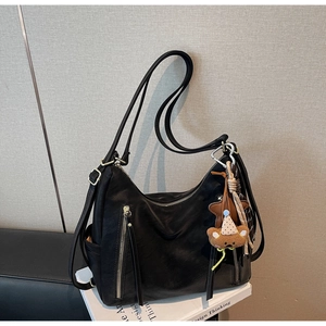 Détail d'un sac cabas en cuir souple noir avec fermeture éclair verticale et charm d'ours
