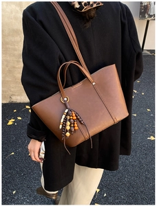 Dettaglio borsa tote in pelle marrone con nappa in perline di legno in ambiente autunnale