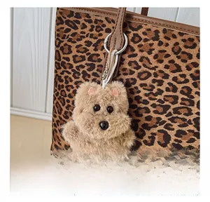 Detailed close-up of a fluffy brown animal charm hanging on a leopard print tote bag