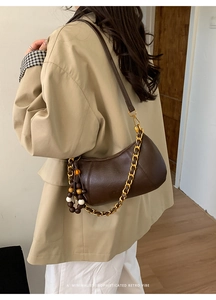 Détail du sac demi-lune marron avec chaîne dorée et perles sur un trench-coat beige