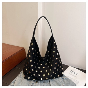 Close-up of black suede tote bag with dense gold rivet studs on blue denim jacket