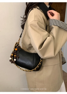 Détail du sac hobo en cuir noir avec chaîne dorée et perles porté sur un trench-coat