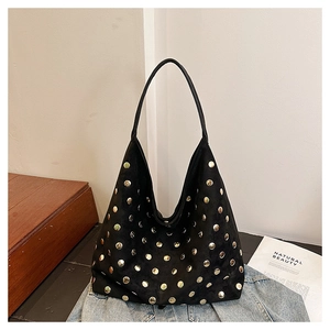 Detail shot of a black suede hobo bag with gold metal studs on a wooden surface