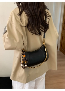 Détail du sac selle en cuir grainé noir avec chaîne dorée et charm perlé sur modèle