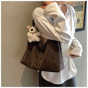 Detail of dark brown faux suede tote bag with white double stitching and teddy bear charm