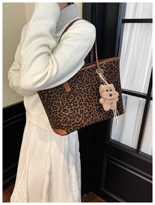 Detail of leopard print tote bag with brown leather handles and plush bear charm