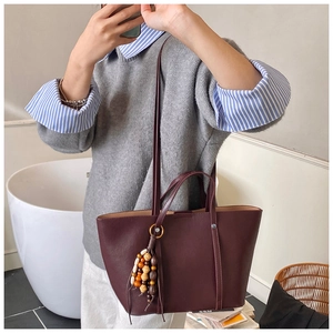 Deep burgundy tote bag detail showing matte leather texture and colorful wood bead charm