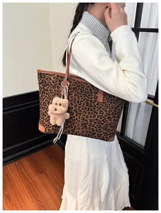 Detail view of leopard print tote bag featuring brown leather trim and plush bear charm