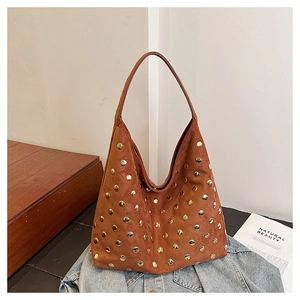Detailed view of a brown suede hobo bag featuring decorative metal rivets on a denim jacket