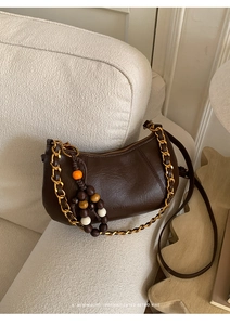 Détail d'un sac demi-lune vintage café noir avec chaîne dorée et breloques en perles