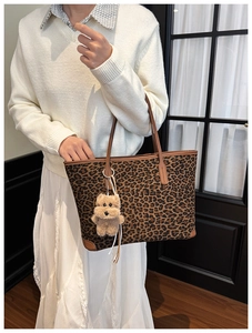 Detail of leopard print tote bag featuring brown leather handles and a plush bear charm