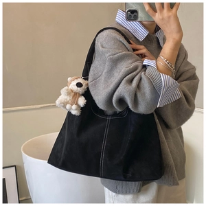 Detail of black suede tote bag featuring white contrast stitching and a plush bear charm