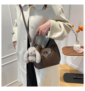 Close-up of brown litchi pattern leather bucket bag with silver buckle and rabbit charm