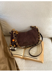 Détail du sac hobo en daim marron foncé avec breloque en bois posé sur des livres anciens