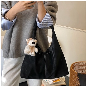 Detail of black leather tote bag with white contrast stitching and plush bear charm