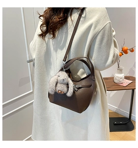 Detail of dark brown lychee leather bucket bag with cute grey plush rabbit charm