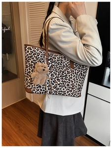 Detail of leopard print tote bag with brown leather handles and a plush bear pendant