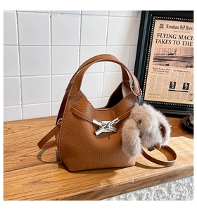 Brown litchi grain leather bucket bag featuring a silver buckle and plush rabbit charm