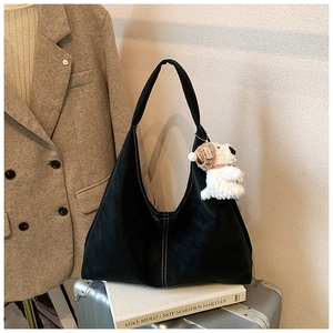 Detail of black suede hobo tote bag featuring contrast stitching and plush dog charm