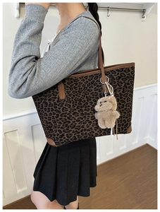 Detail of large leopard print tote bag with brown leather handles and plush bear charm
